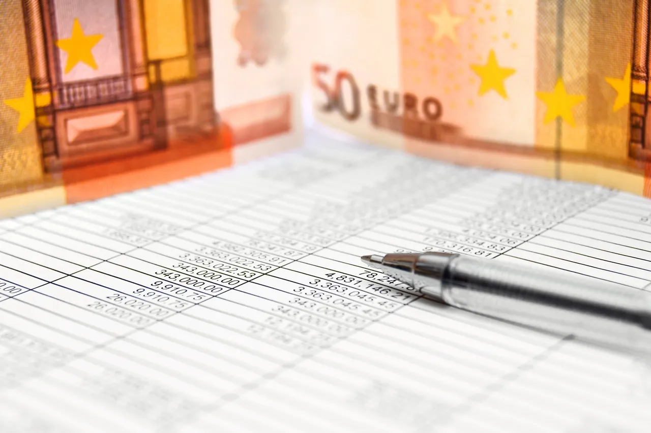 Ein silberner Stift liegt auf einer Tabelle mit Zahlen vor dem Hintergrund einer 50-Euro-Banknote.