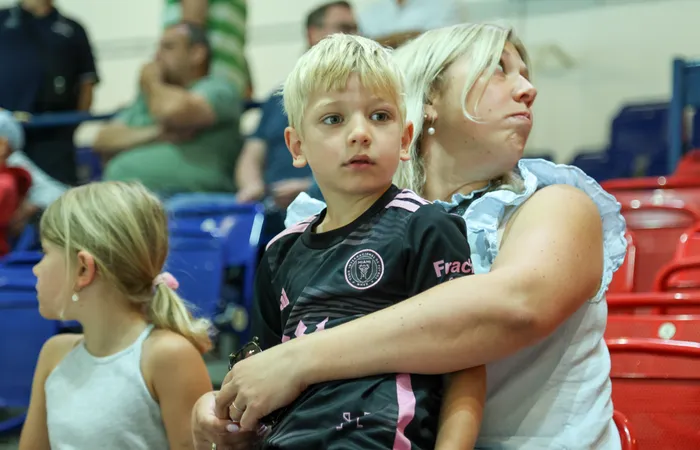 Ein kleiner Junge im schwarz-rosa Trikot der Iserlohn Roosters wird von einer Frau umarmt.