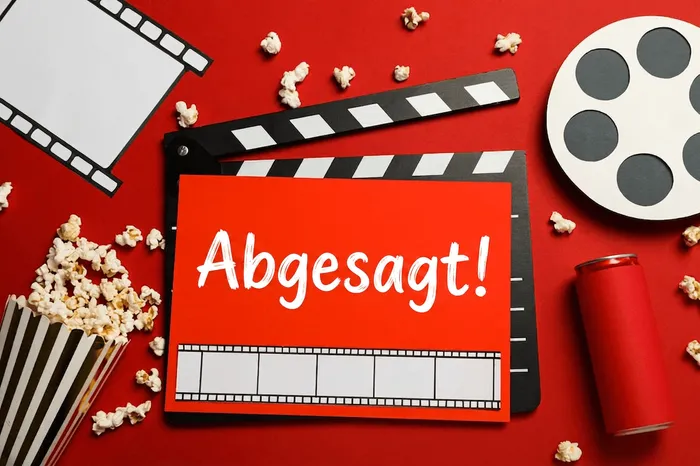 Filmklappe mit dem Schriftzug „Abgesagt!“, Popcorn und Filmrolle auf rotem Hintergrund.
