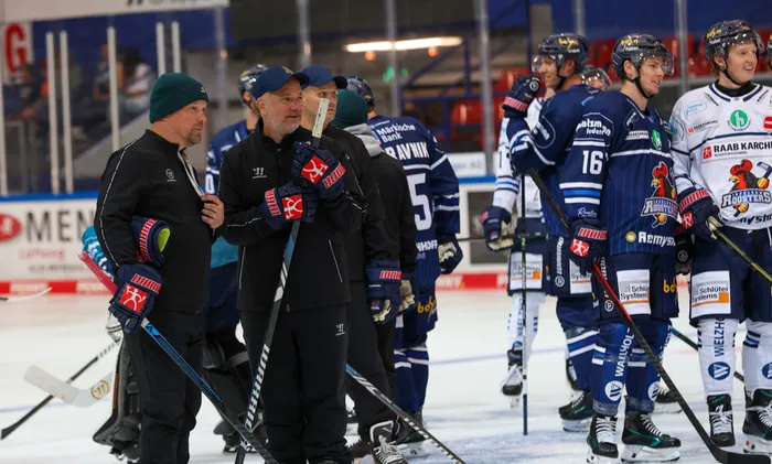 Trainer und Spieler der Iserlohn Roosters stehen mit Eishockeyausrüstung auf dem Eis.