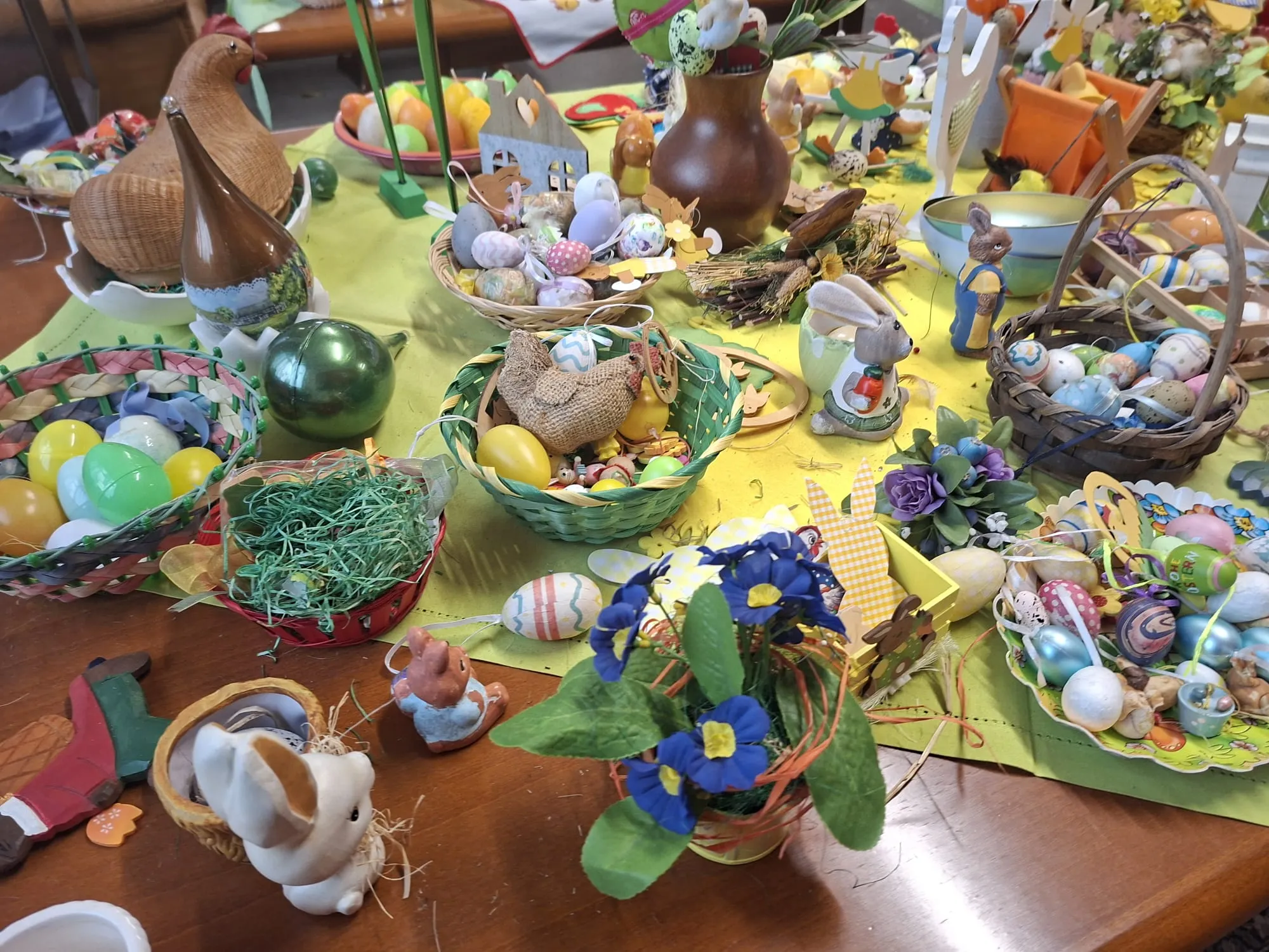 Üppig dekorierter Ostertisch mit bunten Ostereiern, Hasenfiguren, Frühlingsblumen und verschiedenen Körben.