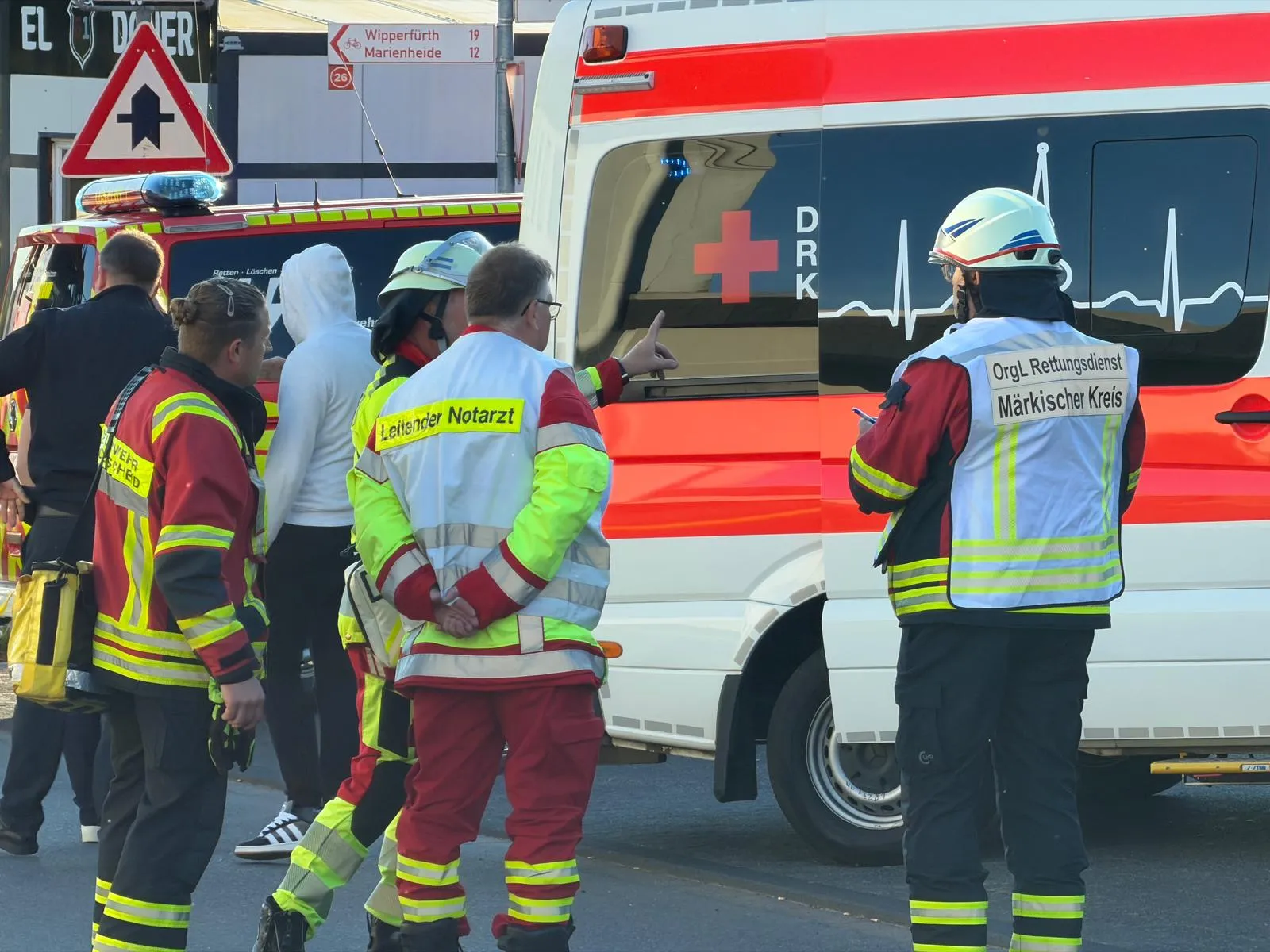 Rettungskräfte in Einsatzkleidung beraten sich vor einem Rettungswagen mit dem Logo des Deutschen Roten Kreuzes am Einsatzort.