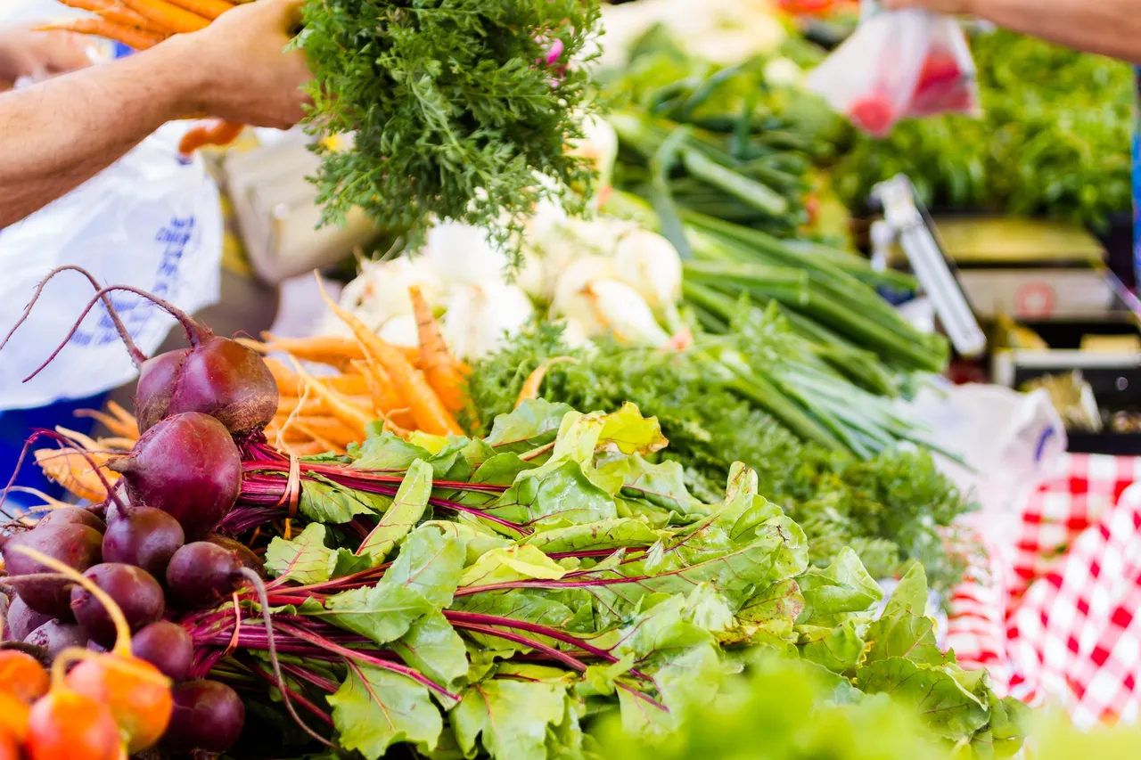 Frisches Gemüse und Kräuter in leuchtenden Farben auf einem Markttisch, darunter Rote Bete, Karotten und verschiedene Salatsorten.