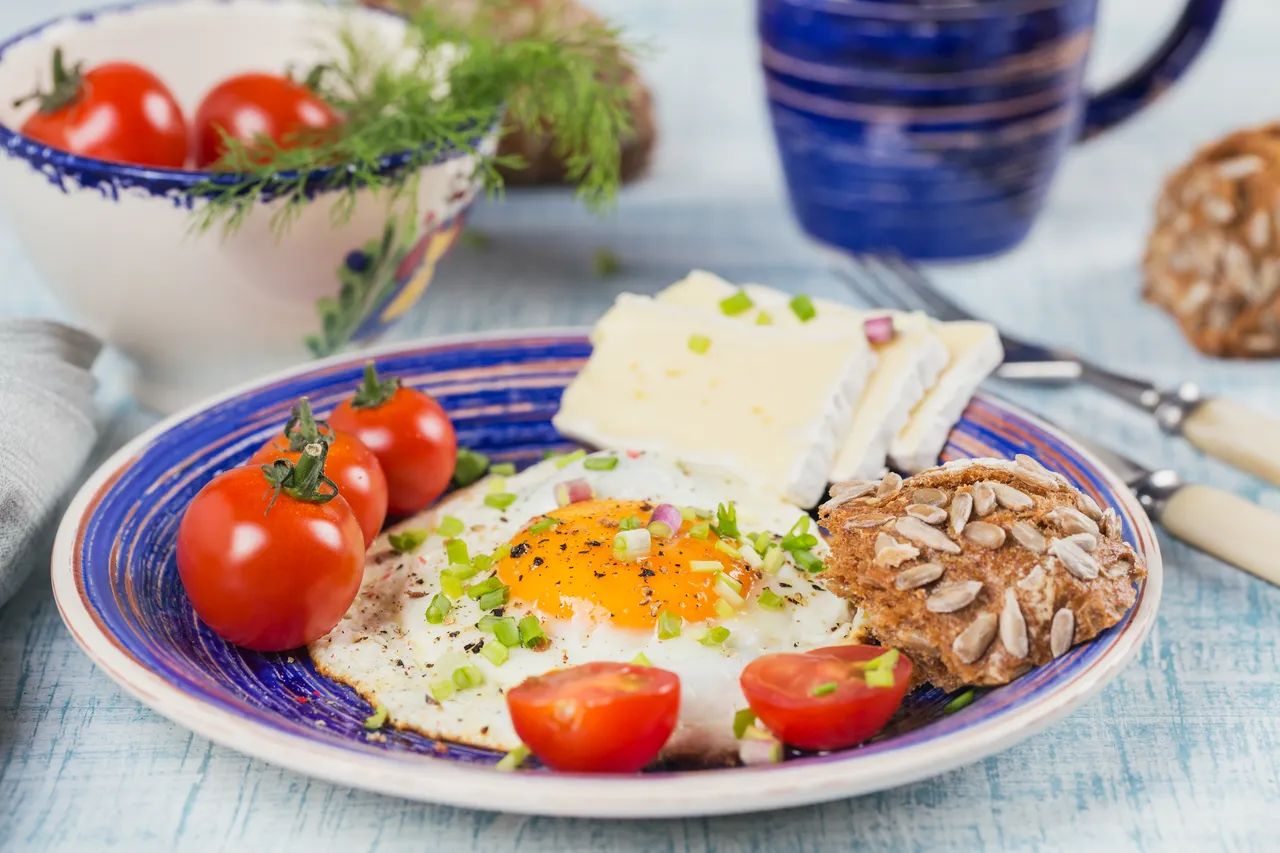 Spiegelei mit Kirschtomaten, Käse und Vollkornbrot auf einem blauen Teller.