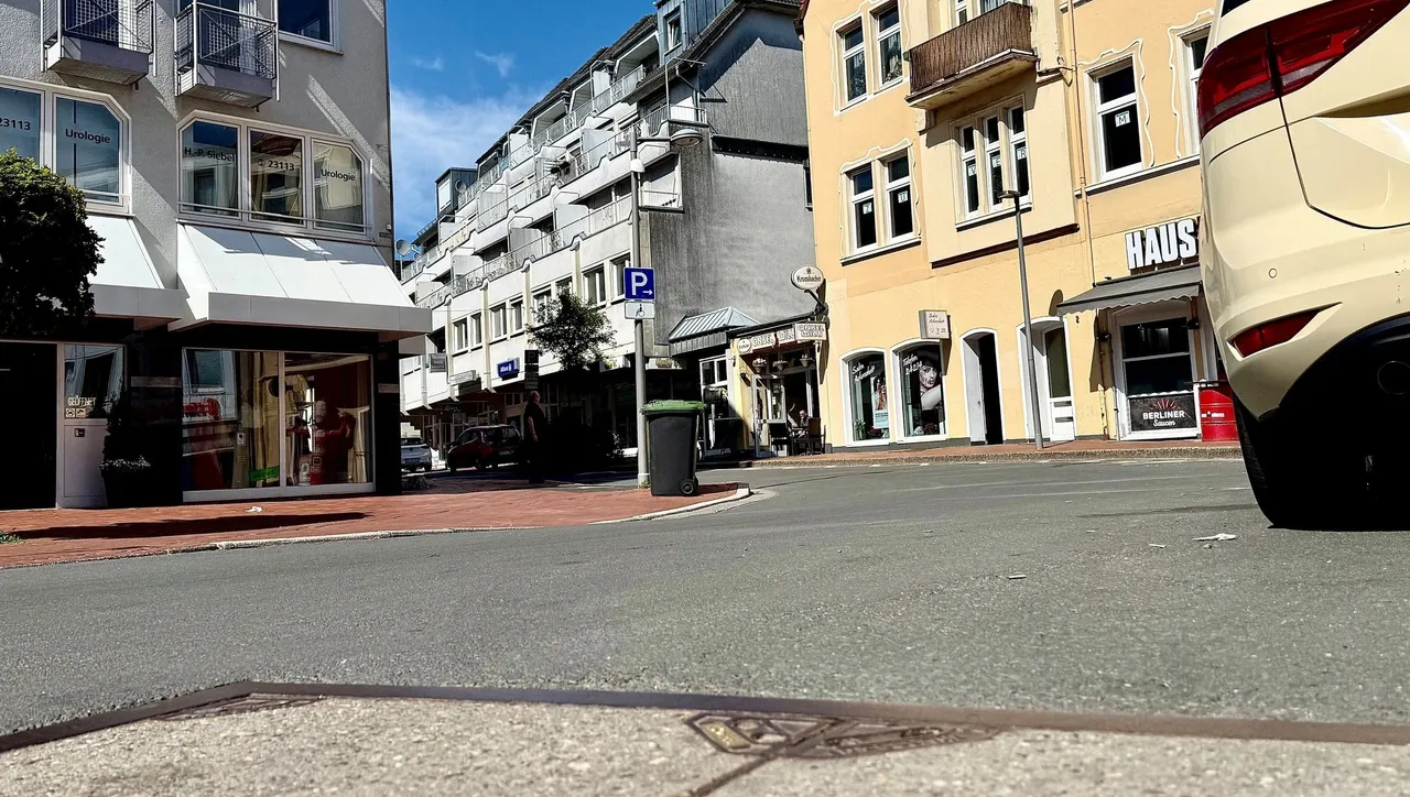 Blick auf die Friedrichstraße mit Geschäften und Häusern, im Vordergrund ein Pflastersteinweg und ein schwarzer Pkw. Im Hintergrund ein Hinweisschild auf eine Parkmöglichkeit.