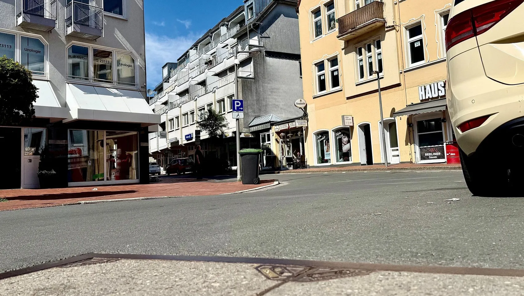 Blick auf die Friedrichstraße mit Geschäften und Häusern, im Vordergrund ein Pflastersteinweg und ein schwarzer Pkw. Im Hintergrund ein Hinweisschild auf eine Parkmöglichkeit.