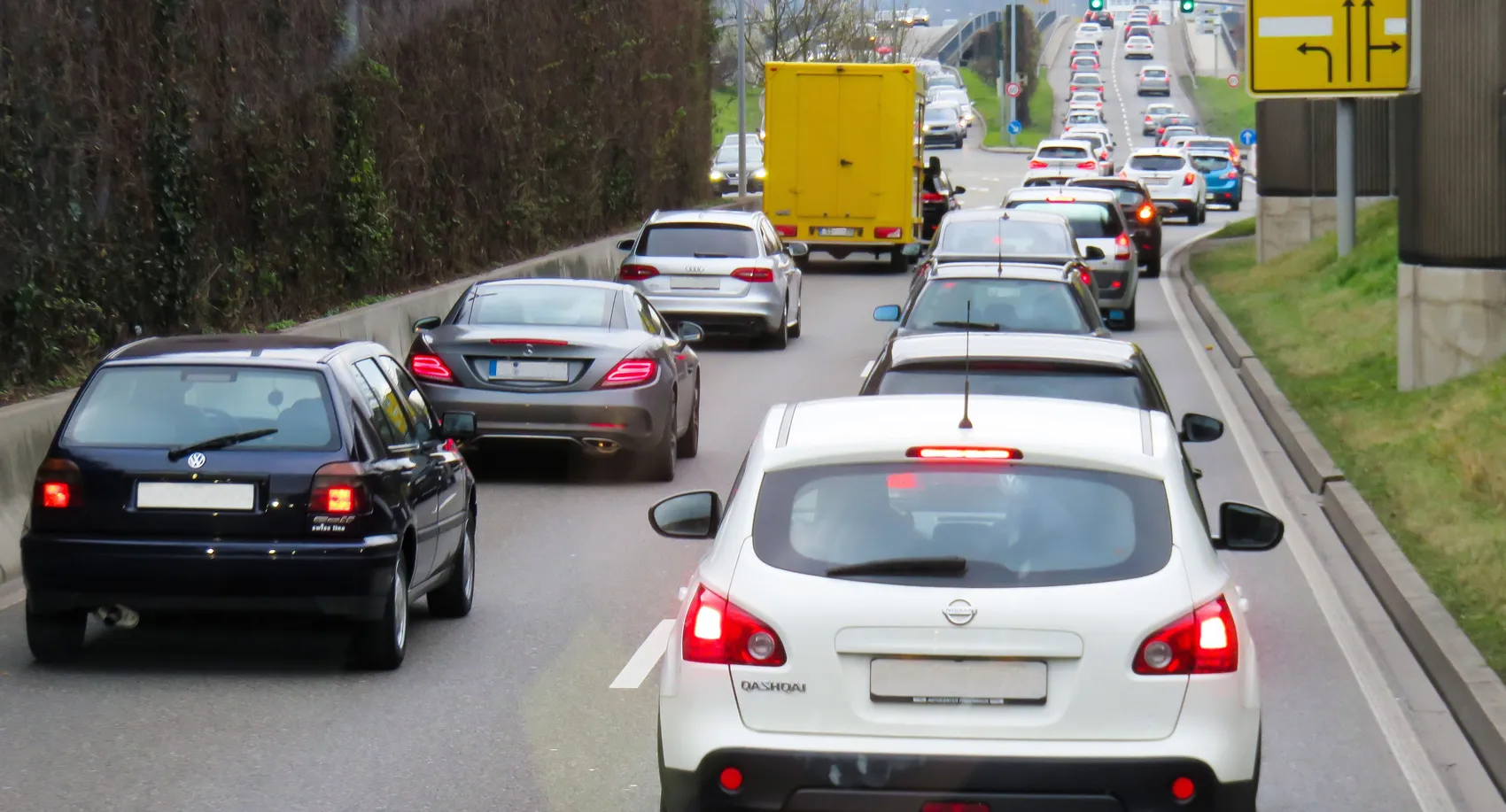 Mehrere Pkw und ein gelber LKW im dichten Verkehr auf einer mehrspurigen Straße.