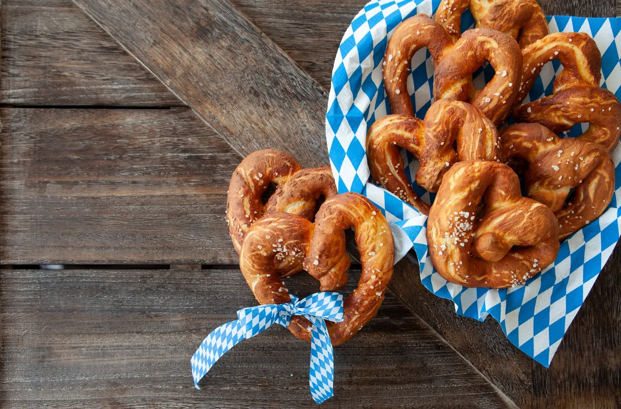 Goldbraune Brezeln auf einem blau-weiß karierten Tuch, eine Brezel im Vordergrund ist mit einer blau-weiß karierten Schleife gebunden.
