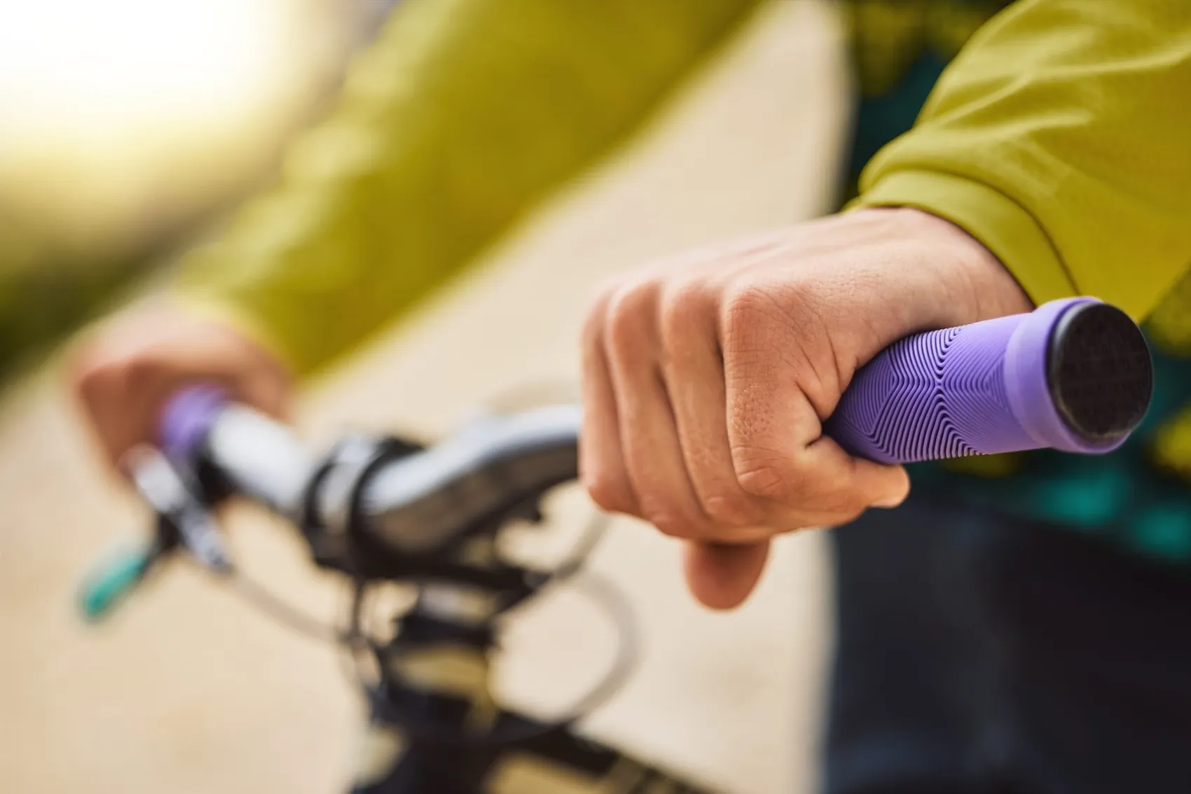 Hände halten einen violetten Fahrradlenker fest, während die Sonne im Hintergrund scheint.