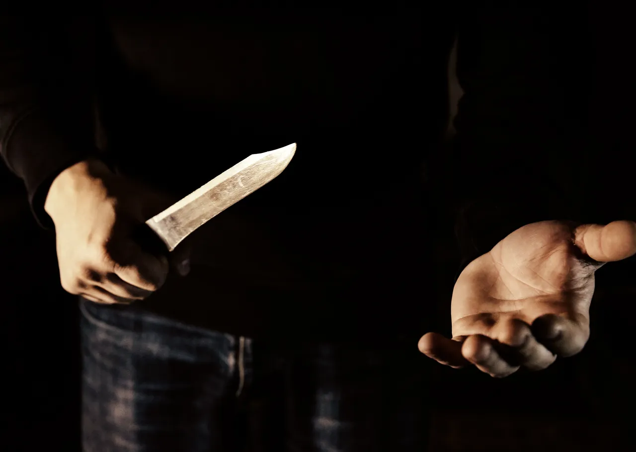 Eine Person in dunkler Kleidung hält ein Messer und streckt die andere Hand offen aus.