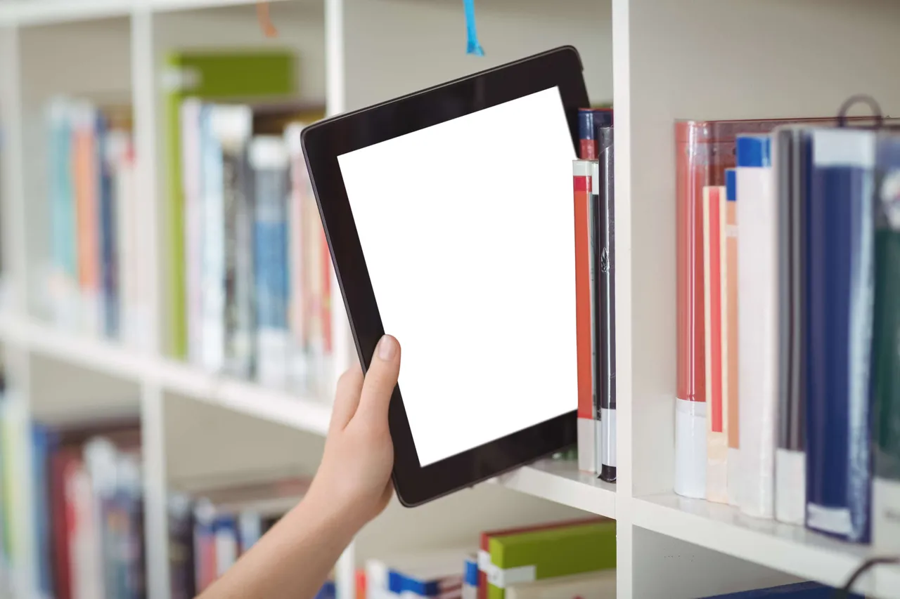 Hand hält Tablet mit leerem Bildschirm vor Bücherregal, symbolisch für digitale Onleihe.