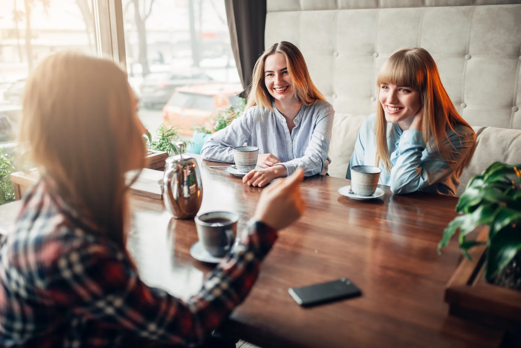 Drei junge Frauen sitzen an einem Holztisch in einem Café und unterhalten sich bei Kaffee.