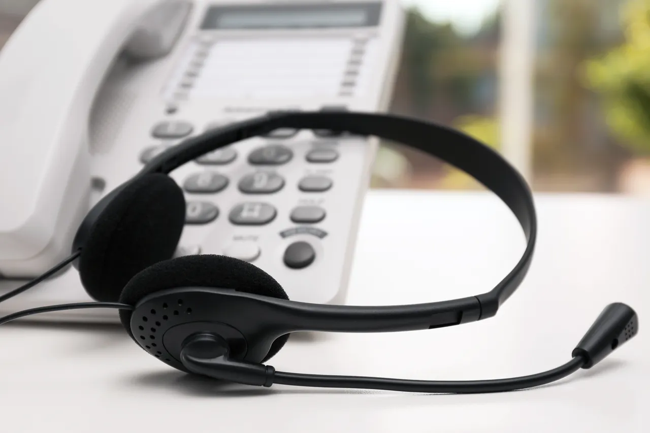 Headset vor einem weißen Telefon auf einem Schreibtisch. Das Bild symbolisiert eine Hotline oder einen Kundenservice.