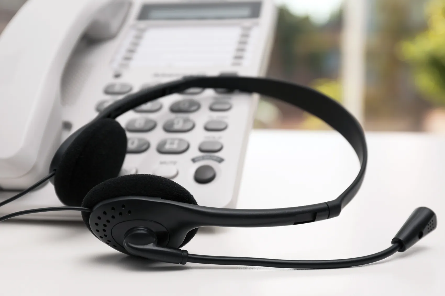 Headset vor einem weißen Telefon auf einem Schreibtisch. Das Bild symbolisiert eine Hotline oder einen Kundenservice.