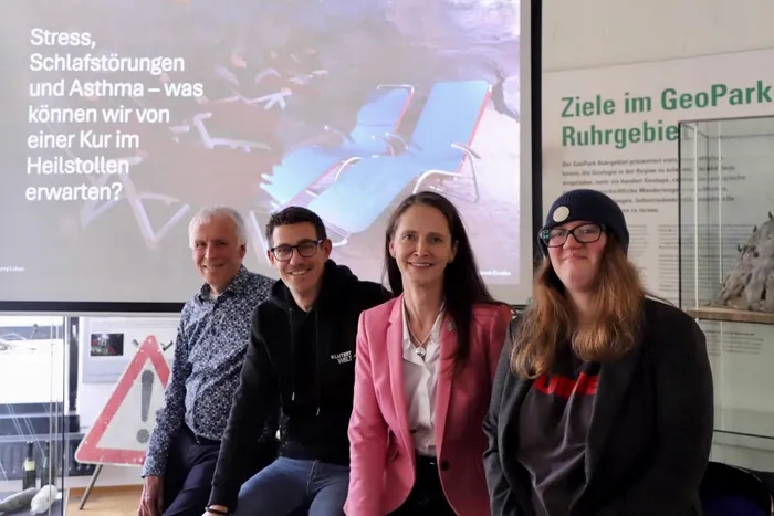 Vier Personen lächeln vor einer Präsentationsfolie über die Wirkung von Heilstollen auf Stress, Schlafstörungen und Asthma.