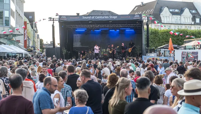 Eine große Menschenmenge beobachtet eine Live-Band auf einer beleuchteten Bühne bei einem Open-Air-Konzert.