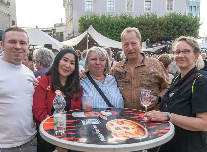 Eine Gruppe von fünf lächelnden Menschen steht hinter einem runden Tisch mit Pizza-Motiv bei der italienischen Nacht in Lüdenscheid.