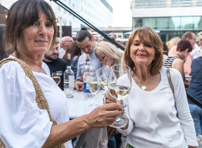 Zwei lächelnde Frauen halten ein Glas Weißwein bei der italienischen Nacht in Lüdenscheid hoch.