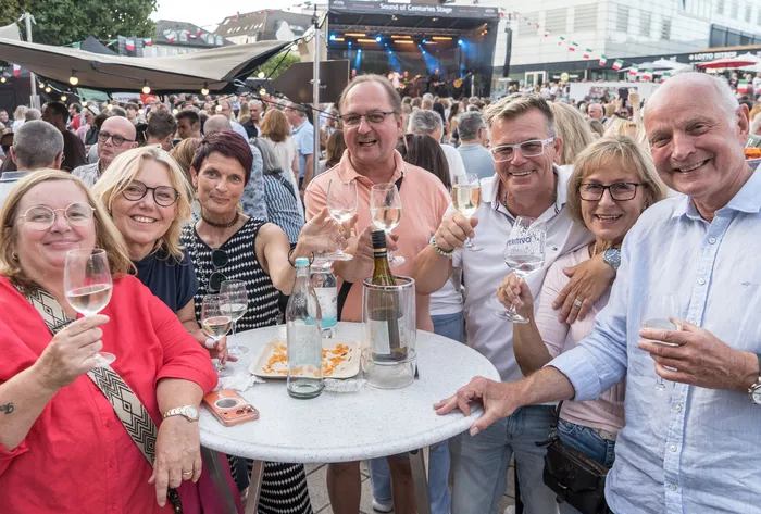 Eine Gruppe lächelnder Menschen stößt bei der italienischen Nacht in Lüdenscheid mit Weingläsern an einem Tisch im Freien an.