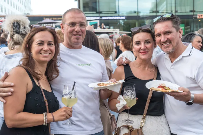 Vier lächelnde Personen halten Getränke und Pizza bei der italienischen Nacht in Lüdenscheid.