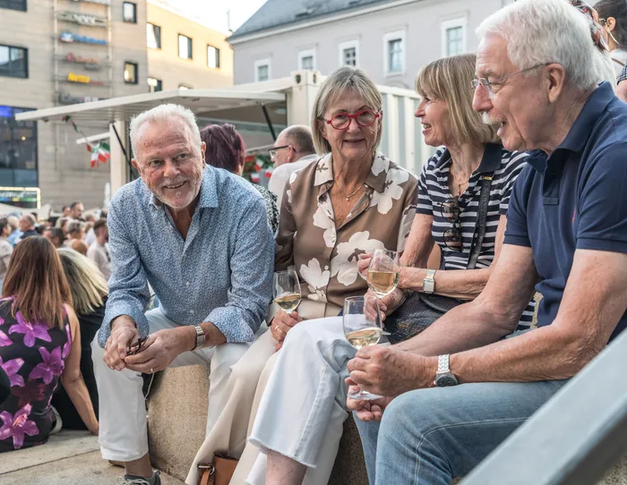 Vier ältere Menschen sitzen bei der italienischen Nacht in Lüdenscheid zusammen und trinken Weißwein.