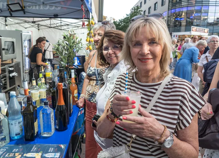 Eine lächelnde Frau mit gestreiftem Oberteil hält ein Getränk an einem Stand mit zahlreichen Flaschen bei der italienischen Nacht in Lüdenscheid.