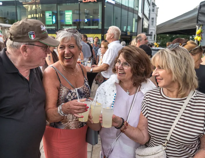 Eine Gruppe lachender Menschen hält Gläser mit hellen Getränken bei der italienischen Nacht in Lüdenscheid.