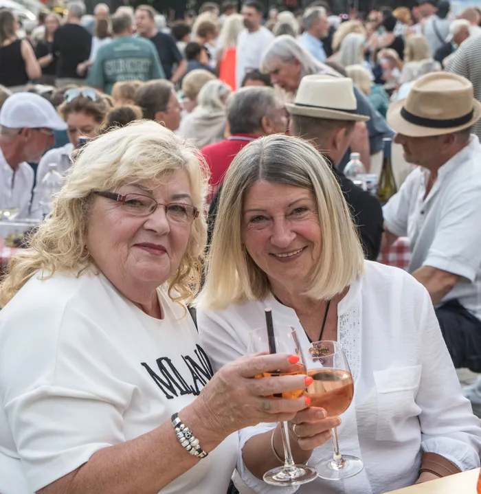 Zwei lächelnde Frauen stoßen mit Gläsern Roséwein an, im Hintergrund sind weitere Gäste bei der italienischen Nacht in Lüdenscheid zu sehen.