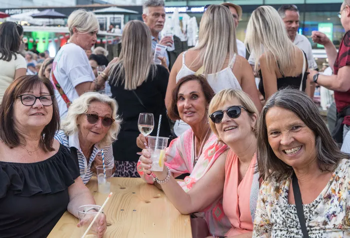 Eine Gruppe lächelnder Frauen sitzt an einem Tisch mit Wein und Cocktails bei der italienischen Nacht in Lüdenscheid.