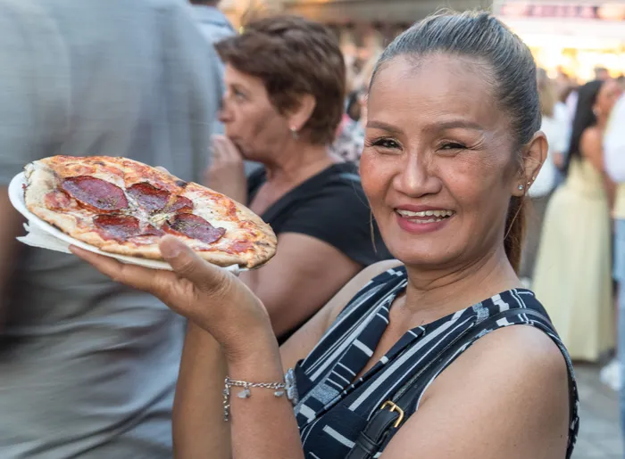Eine lächelnde Frau hält eine Pizza auf einem Teller bei der italienischen Nacht in Lüdenscheid.