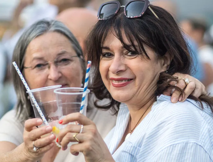 Zwei lächelnde Frauen halten Plastikbecher mit blau-weiß gestreiften Strohhalmen hoch.