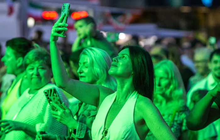 Eine Frau macht mit ihrem Smartphone ein Selfie in einer Menschenmenge bei der italienischen Nacht in Lüdenscheid unter grünem Licht.