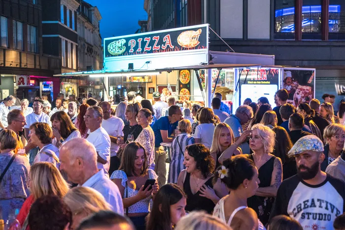 Eine Menschenmenge versammelt sich vor einem beleuchteten Pizza-Imbisswagen während der italienischen Nacht in Lüdenscheid.