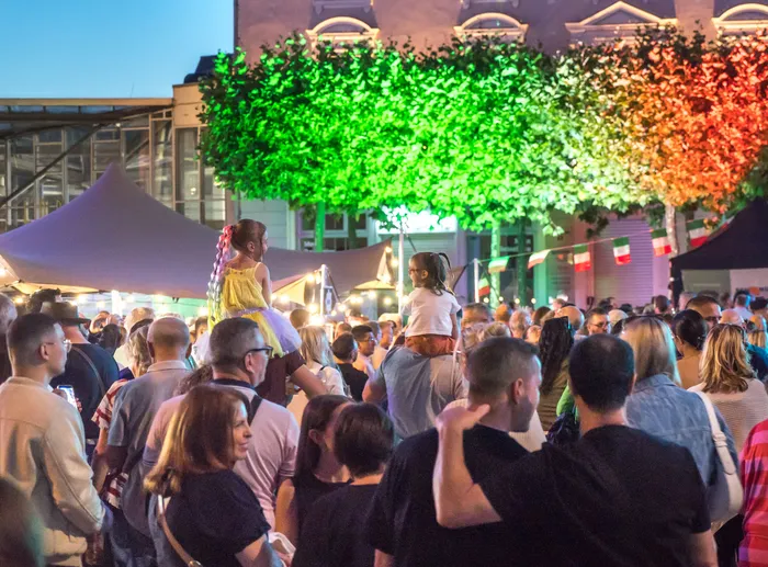 Menschenmenge bei der italienischen Nacht in Lüdenscheid unter einem in den Nationalfarben Grün, Weiß und Rot beleuchteten Blätterdach.