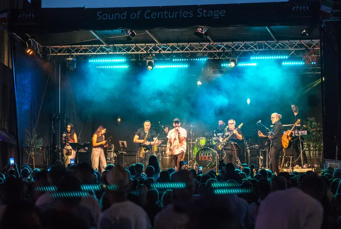 Eine Band spielt unter blauem Bühnenlicht auf der „Sound of Centuries Stage“ vor einem Publikum.