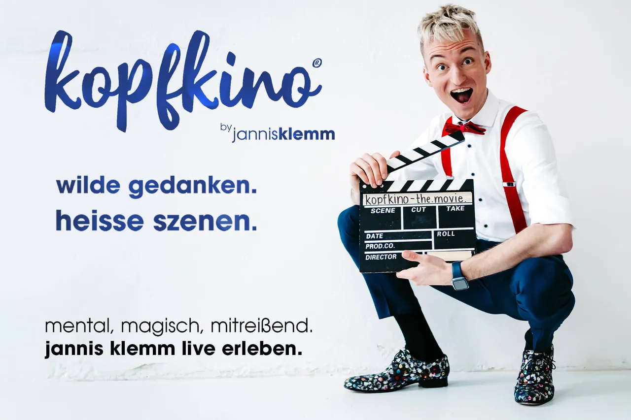Jannis Klemm in Anzug und mit roten Accessoires hält eine Filmklappe mit der Aufschrift „kopfkino – the movie“ in der Hand und lächelt in die Kamera.