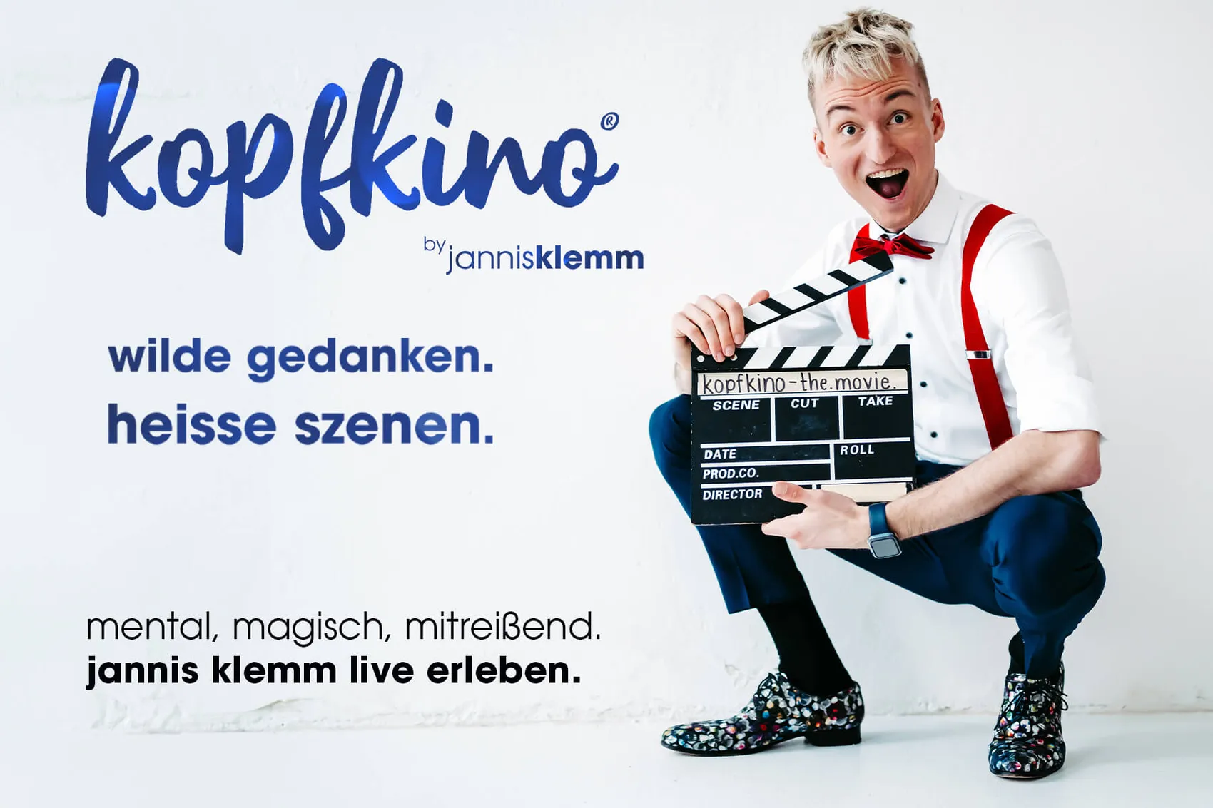 Jannis Klemm in Anzug und mit roten Accessoires hält eine Filmklappe mit der Aufschrift „kopfkino – the movie“ in der Hand und lächelt in die Kamera.