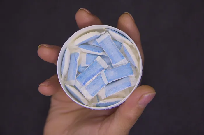 Eine Hand hält eine weiße Dose, die mit kleinen, weiß-blauen Nikotinbeuteln gefüllt ist.