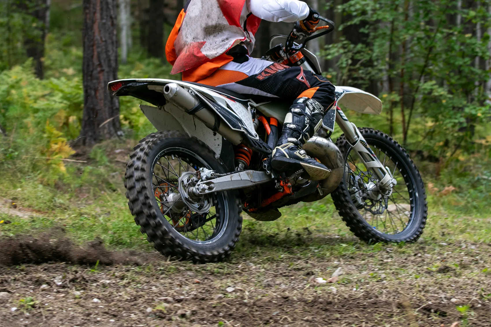 Ein Enduro-Motorrad fährt auf einem Waldweg und wirbelt dabei Erde auf.