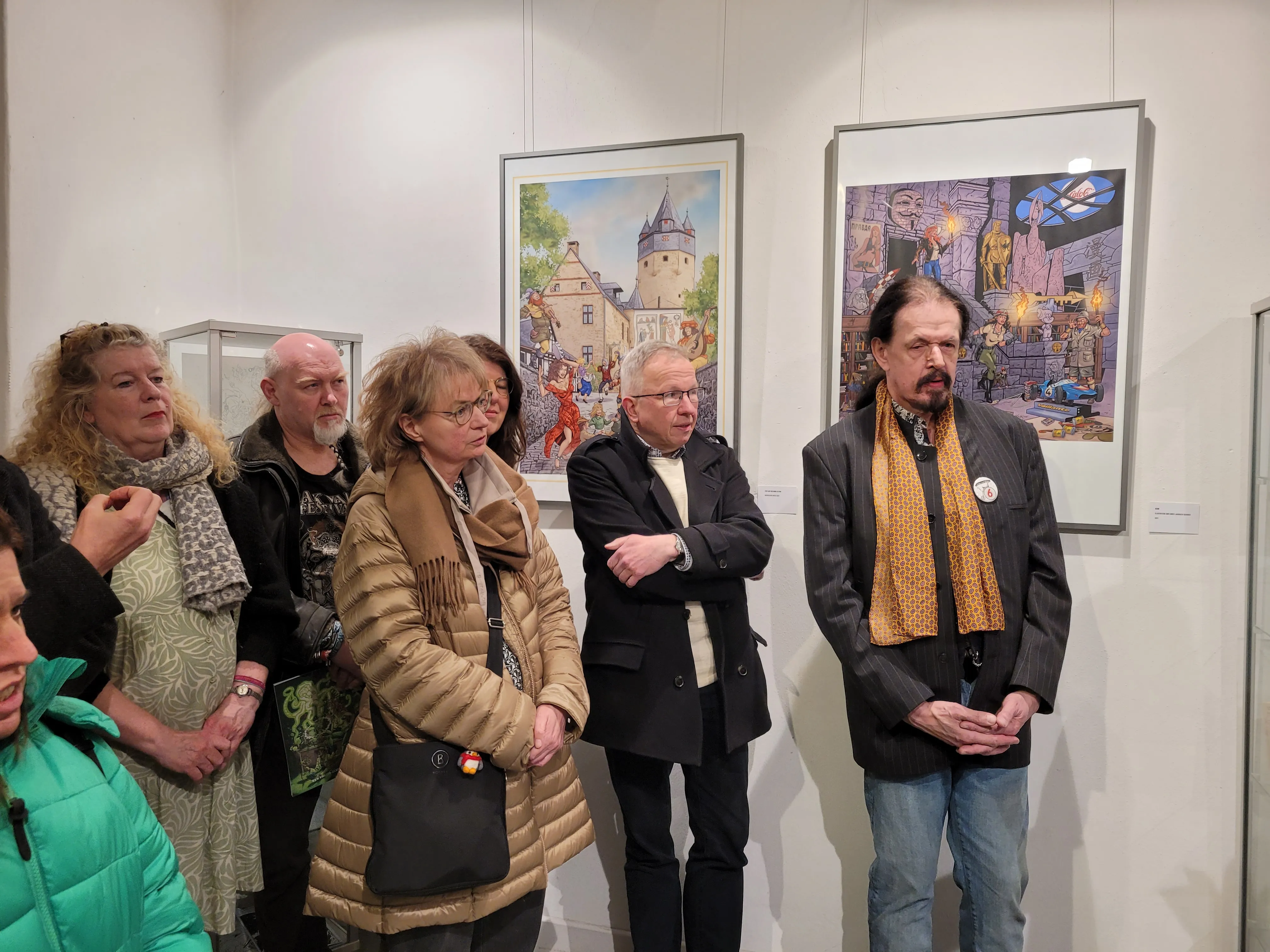 Mehrere Besucher betrachten Gemälde in einer Ausstellung im Heimathaus, darunter eine mittelalterliche Stadtansicht und eine Fantasieszene.