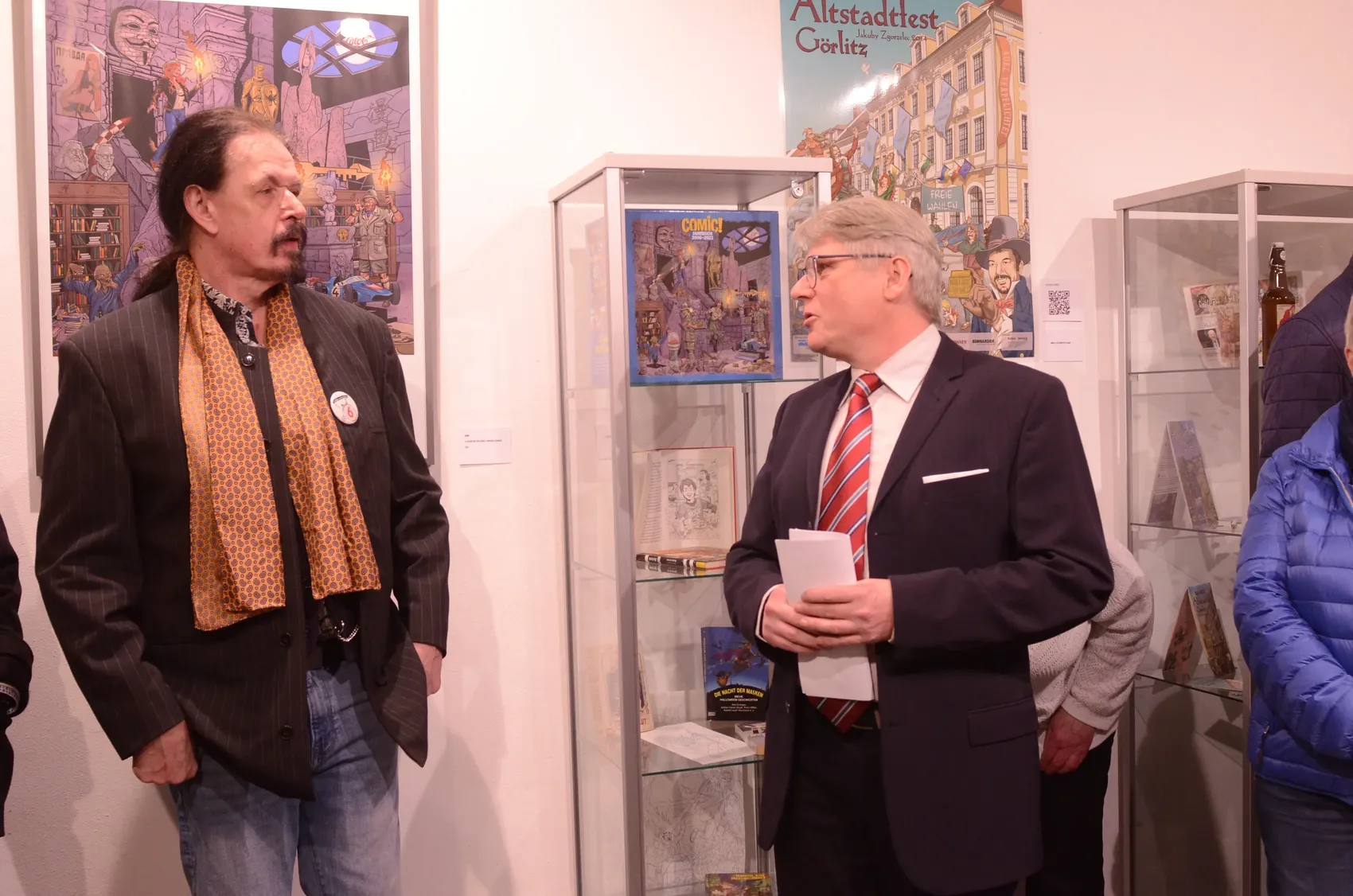 Zwei Männer betrachten Comiczeichnungen in Vitrinen während der Ausstellungseröffnung von Dietmar Krüger im Heimathaus Görlitz.