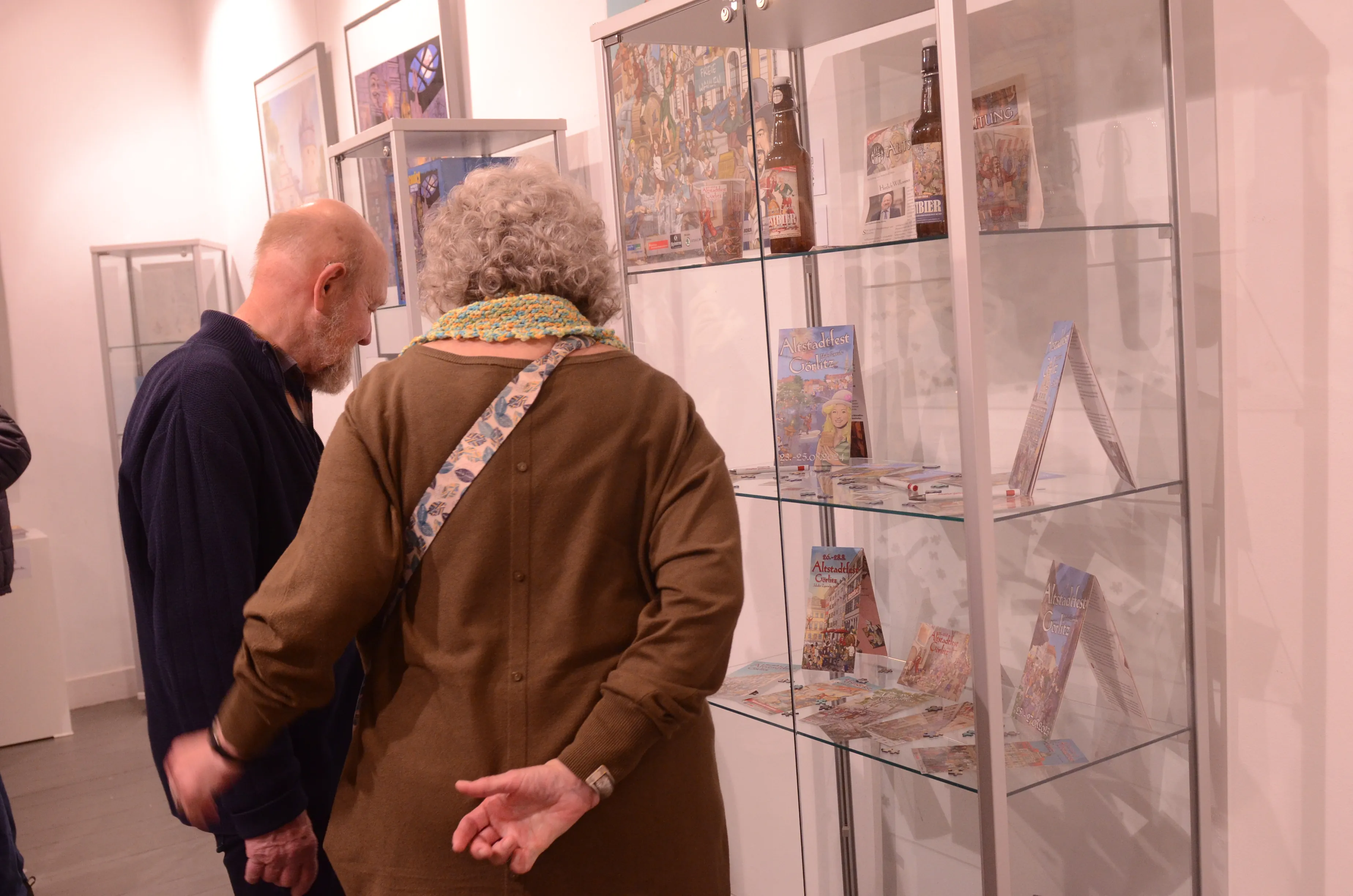 Zwei Besucher betrachten in einer Vitrine ausgestellte Comiczeichnungen und Illustrationen des Künstlers Dietmar Krüger im Heimathaus.
