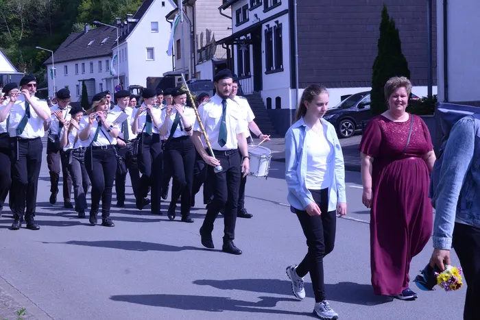 Musikzug mit Blasinstrumenten und Trommler marschiert auf einer Straße, begleitet von Zivilisten, während eines Schützenfestumzugs.