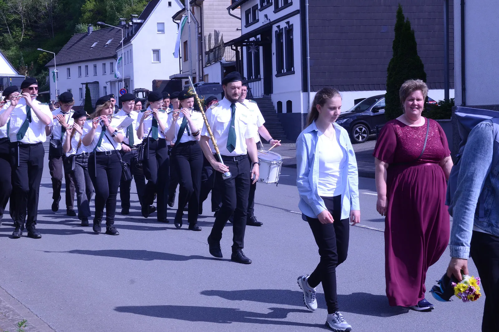 Musikzug mit Blasinstrumenten und Trommler marschiert auf einer Straße, begleitet von Zivilisten, während eines Schützenfestumzugs.