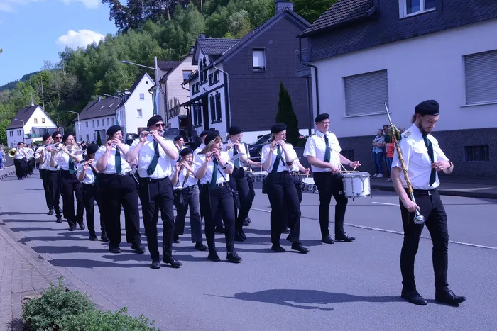 Musikzug mit Blasinstrumenten und Trommlern marschiert auf einer Straße vor Wohnhäusern im Rahmen eines Schützenfestes.