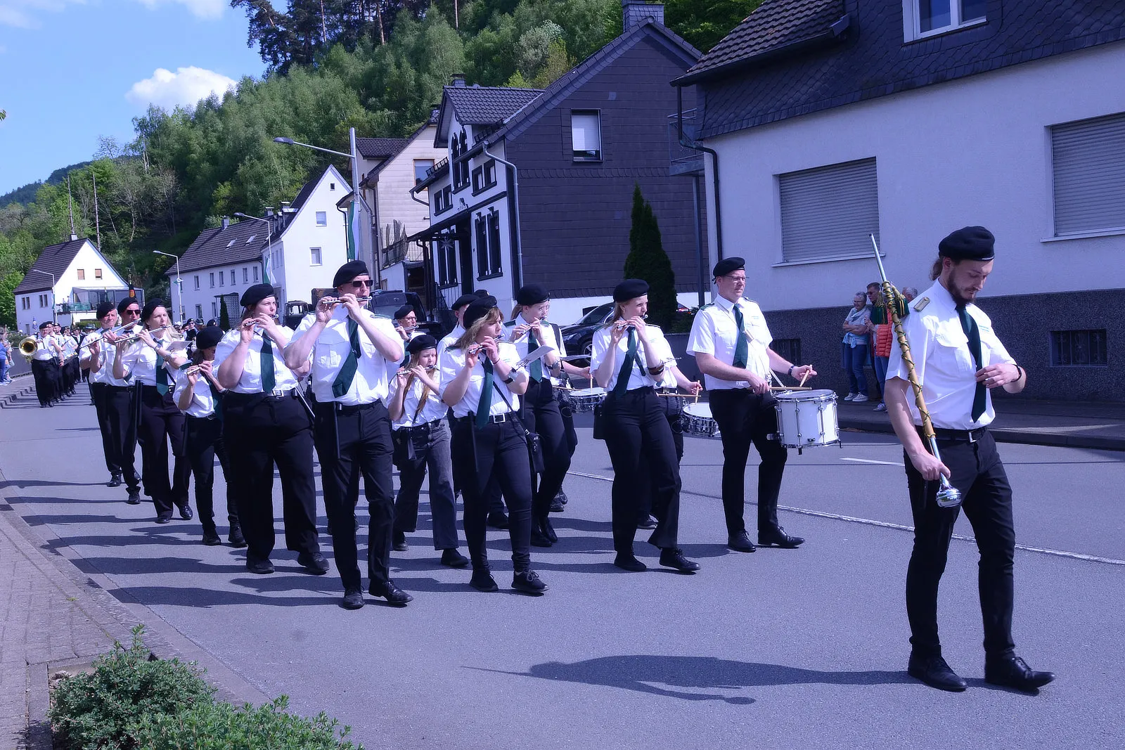 Musikzug mit Blasinstrumenten und Trommlern marschiert auf einer Straße vor Wohnhäusern im Rahmen eines Schützenfestes.
