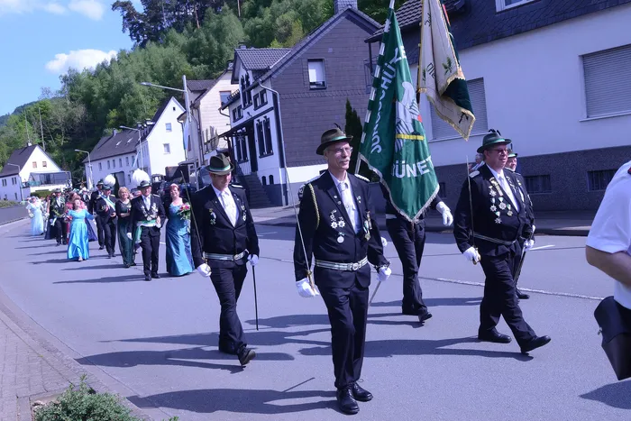 Festzug mit Schützen in historischen Uniformen und einer grün-weißen Fahne durch eine Wohngegend.