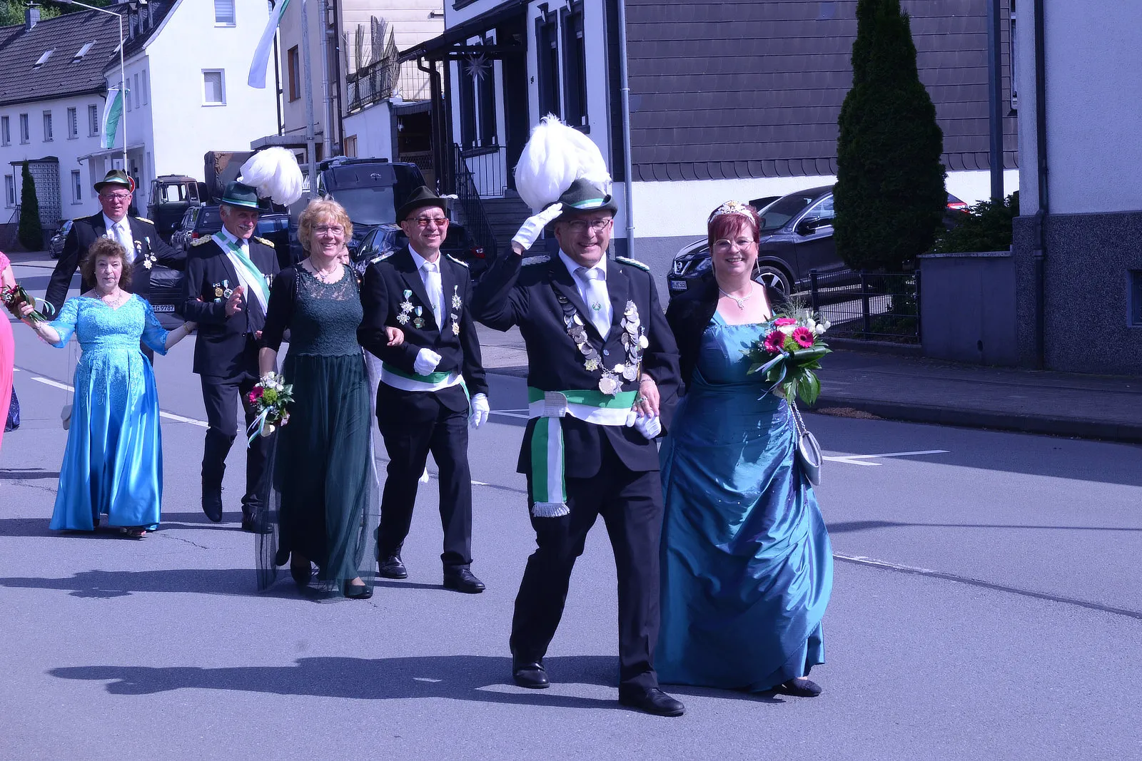 Festumzug mit Schützen in historischen Uniformen und festlich gekleideten Paaren, begleitet von einer Blaskapelle, zieht durch eine Stadtstraße.