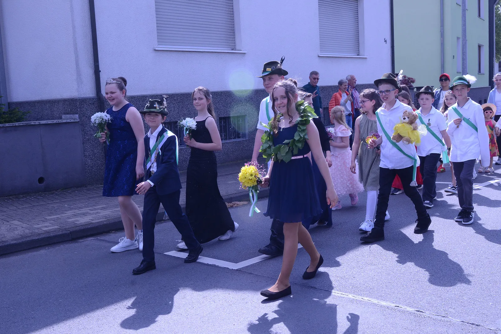 Festumzug mit Kindern und Jugendlichen in Tracht, die Blumen tragen, vor Häusern in Plettenberg.