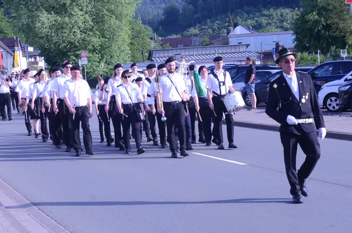 Eine Gruppe von Musiker:innen und Mitgliedern einer Schützenkompanie marschiert auf einer Straße, angeführt von einer Person in historischer Uniform.